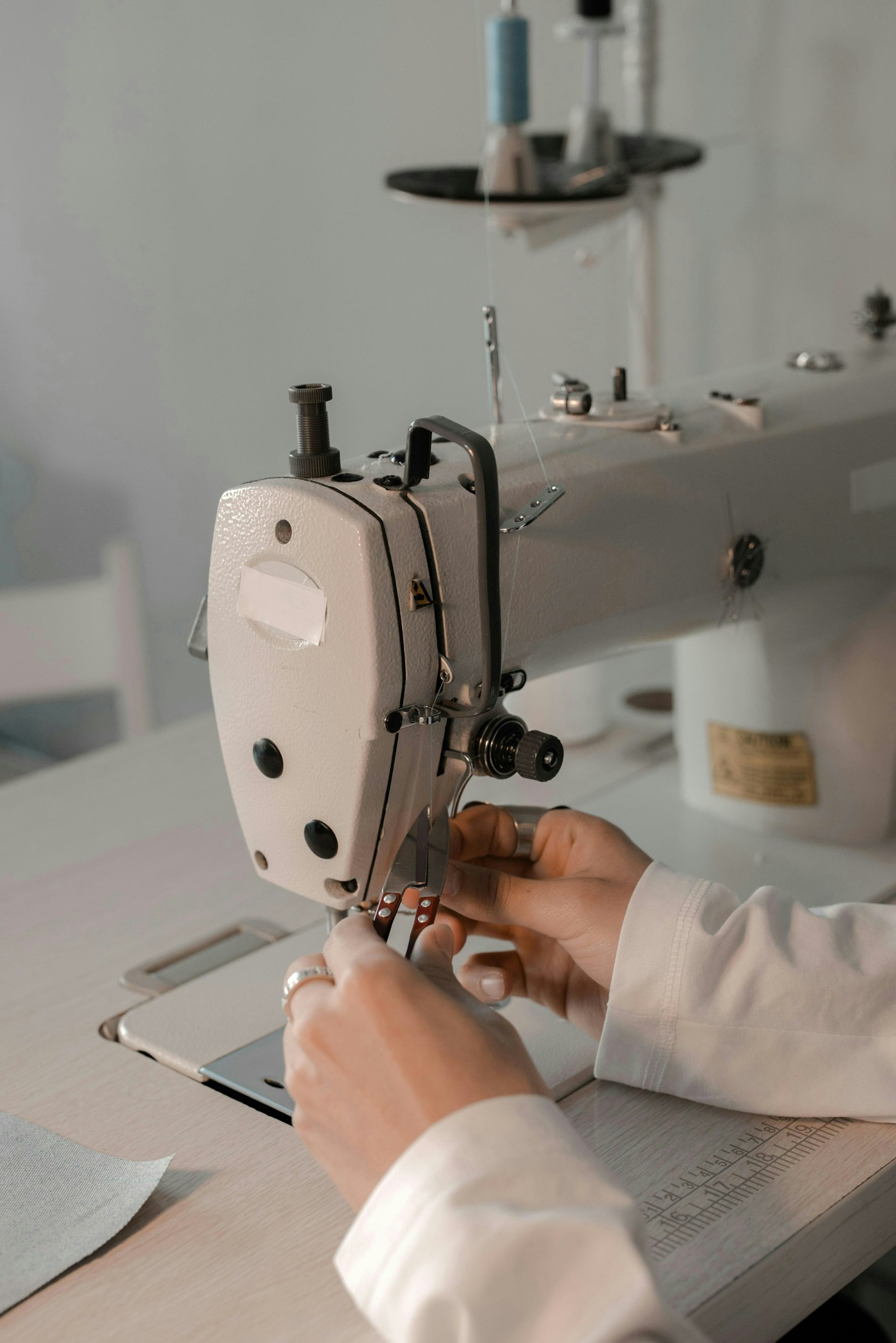 Hands guiding cloth under the presser foot of an industrial flatbed sewing machine, with a steel ruler on the table alongside.
